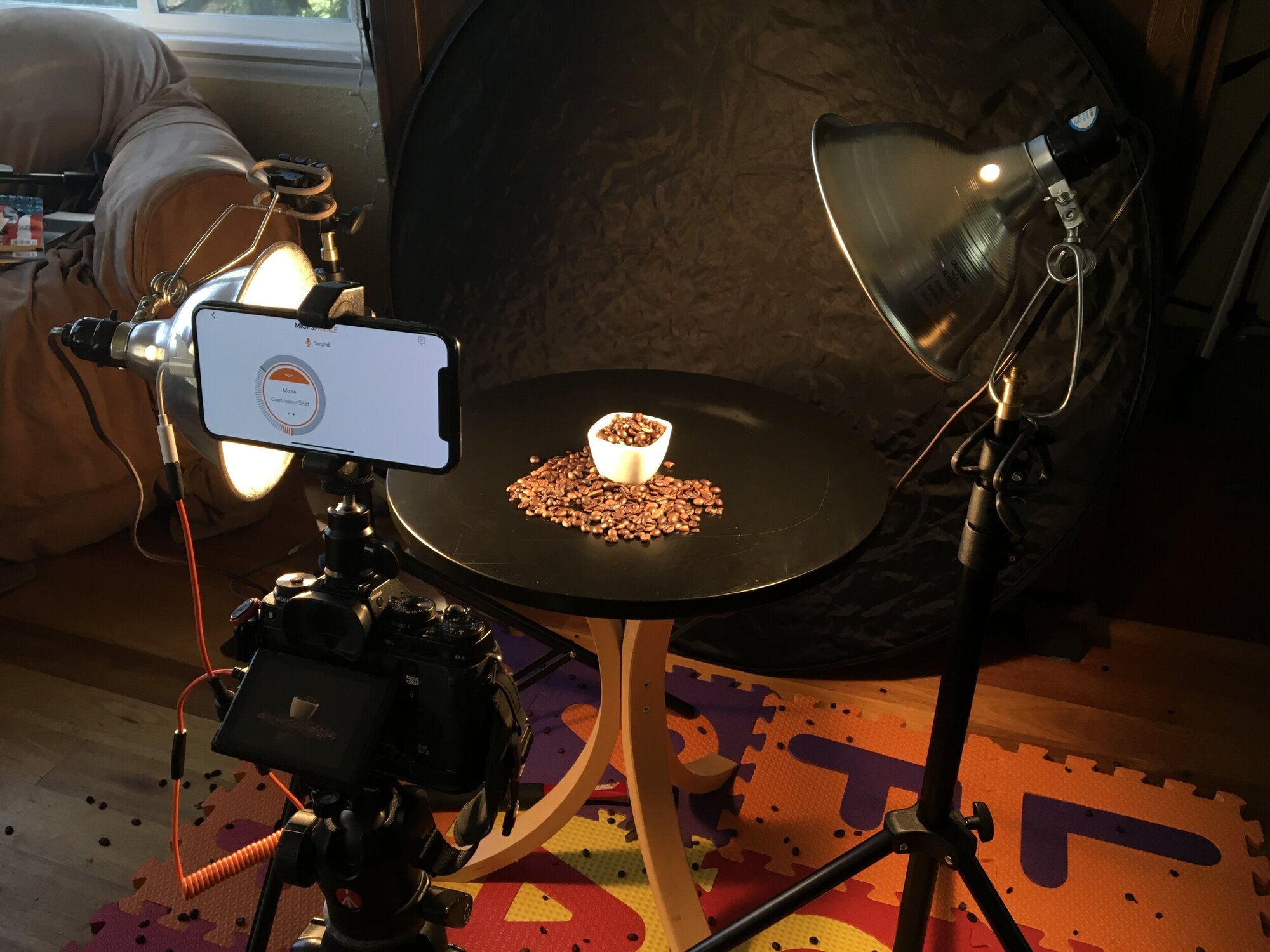 The setup for the jumping coffee beans photo. The MIOPS app was set to trigger the camera’s shutter when the phone’s microphone picked up a loud noise above a specified threshold. That noise came from whacking the underside of the table with a hammer (hence the mat underneath and the smattering of beans all over the floor).